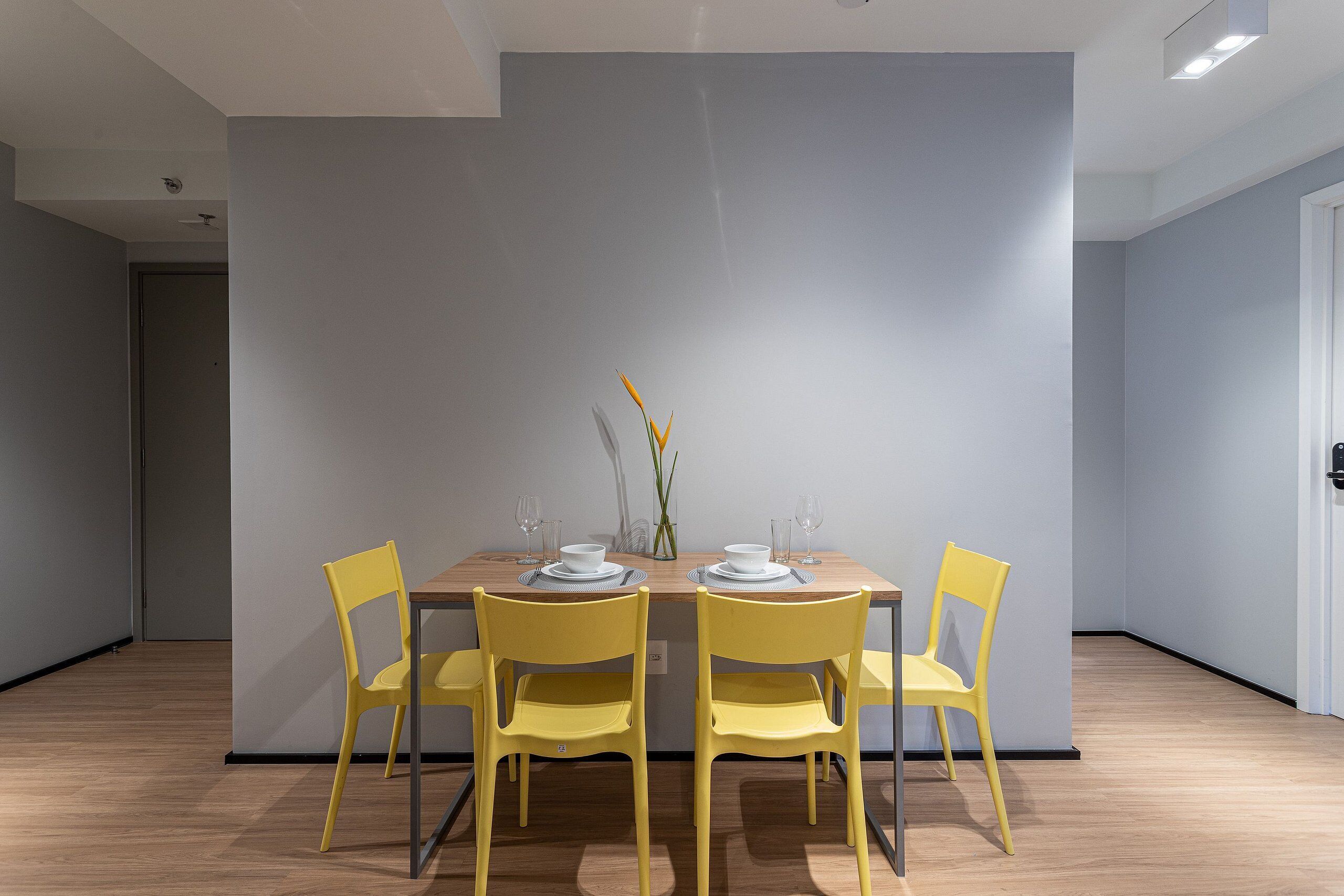 A dining area with a wooden table, four yellow chairs, and a vase with flowers.