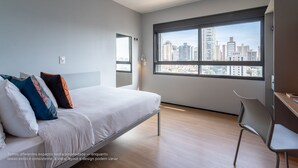Une chambre moderne avec un lit, un bureau et une grande fenêtre donnant sur la ville.