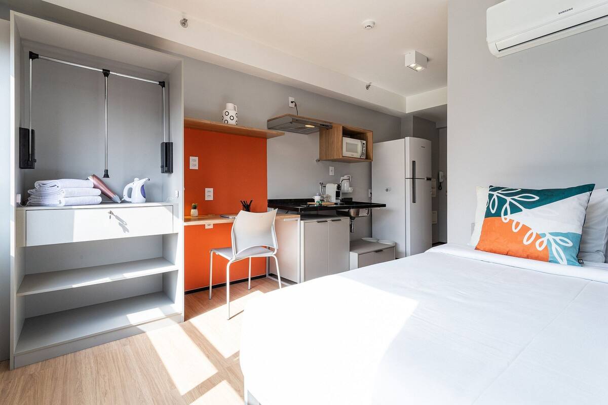 Ein kleines Hotelzimmer mit Bett, Schreibtisch, Stuhl, Mikrowelle und Kühlschrank.