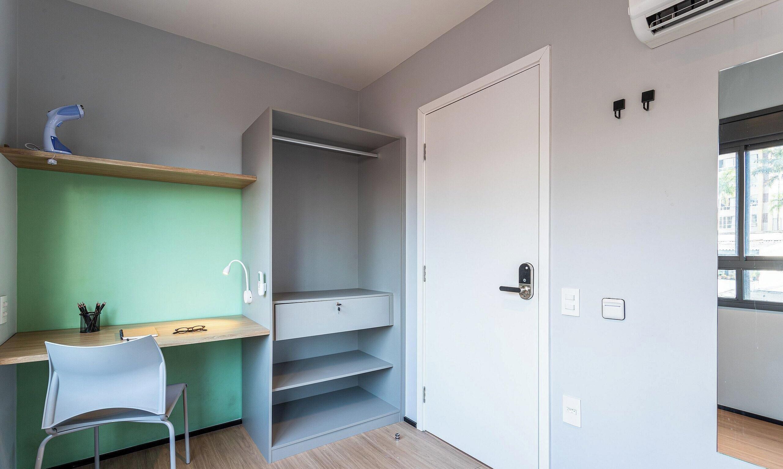A room with a desk, chair, open wardrobe, and a door leading to another room.