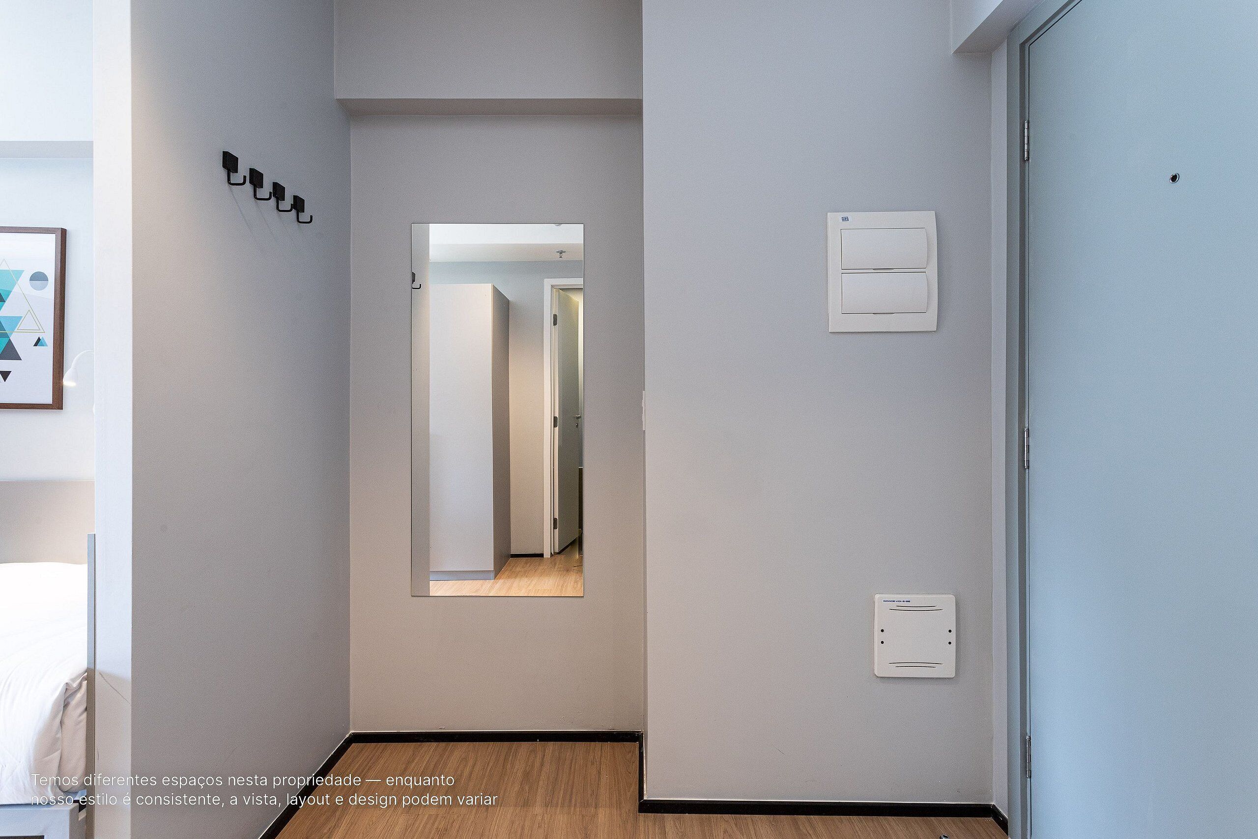 A hallway with a mirror, light switch, and a door.