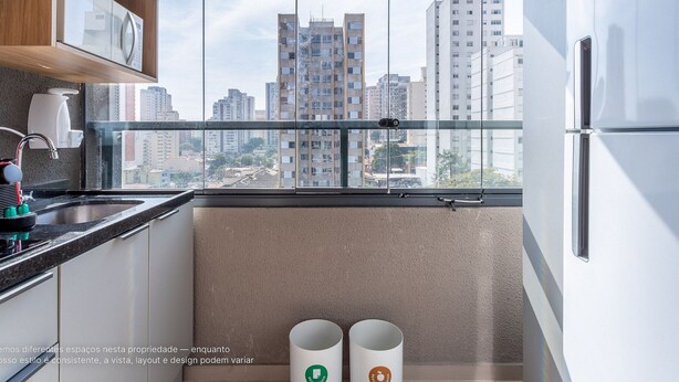 Une cuisine avec vue sur de hauts immeubles, un four à micro-ondes, une machine à café et deux poubelles.