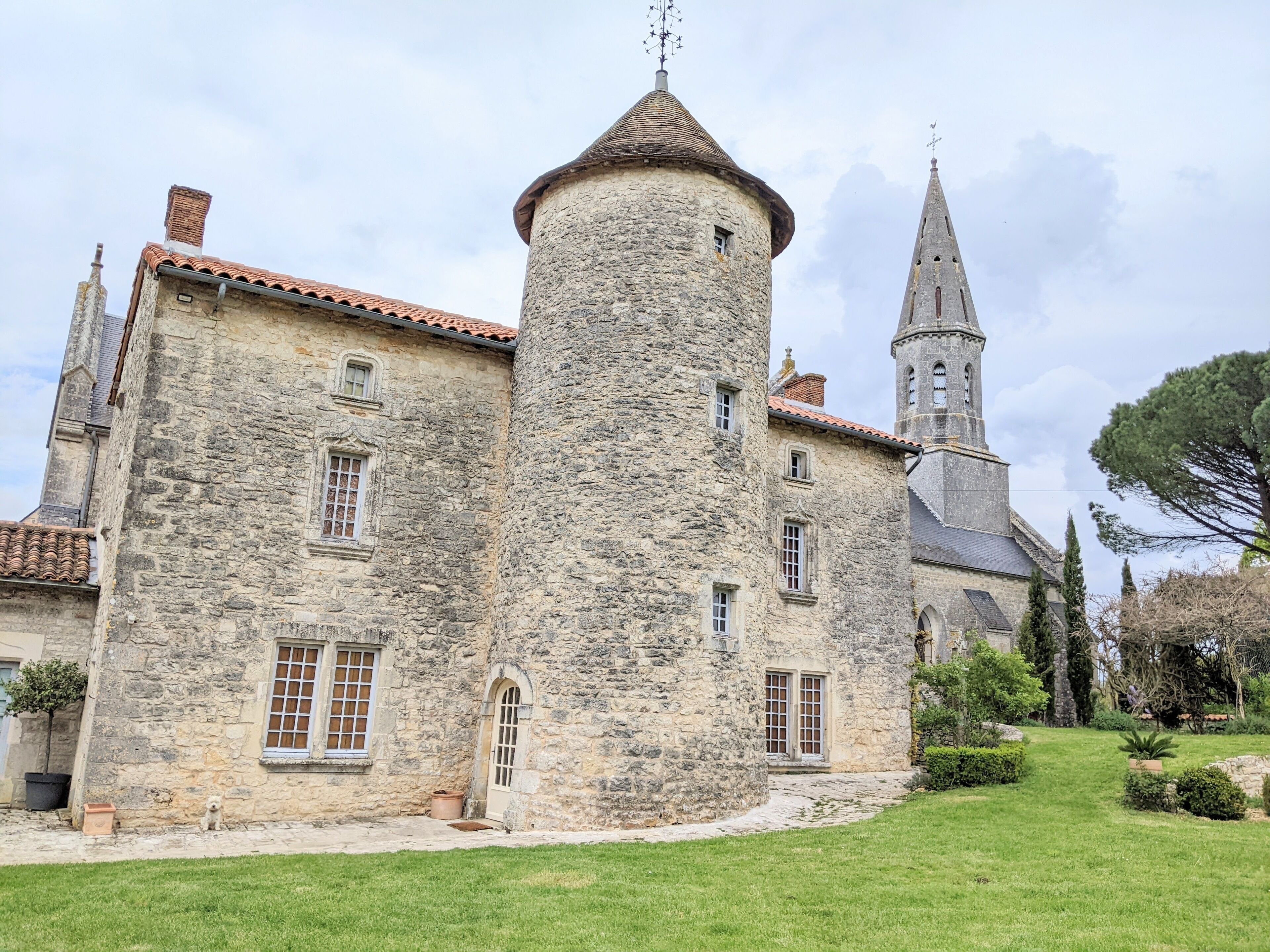 A historic stone building with a central tower, a church steeple, and a well-maintained lawn.
