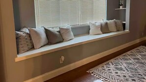 Habitación con un banco empotrado junto a la ventana, decorada con diversos cojines y una estantería ornamental arriba.