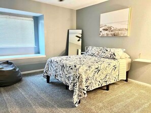 A bedroom with a bed, a bedside table, a mirror, a window with blinds, and a bean bag chair. - Ocean Dr Gem! Walk 2 Bay & Downtown. Spacious! (Corpus Christi)