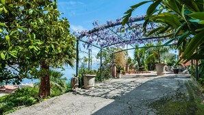 A paved pathway with a pergola covered in purple flowers, leading to a seating area with tables and chairs. - Casetta Amelia With Seaview by Wonderful Italy (Taormina)