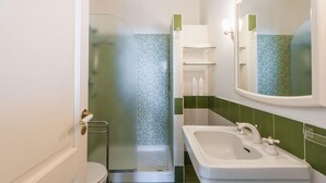 A bathroom with a glass shower enclosure, a white sink with a mirror, and green tiled walls. - Casetta Amelia With Seaview by Wonderful Italy (Taormina)