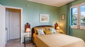 A bedroom with a bed, two bedside tables with lamps, a door, a framed picture on the wall, and a window with a view of the outdoors. - Casetta Amelia With Seaview by Wonderful Italy (Taormina)