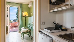 A compact kitchen with a refrigerator, a sink, and a stove. There is a dining area with chairs and a table, and a lamp. - Casetta Amelia With Seaview by Wonderful Italy (Taormina)