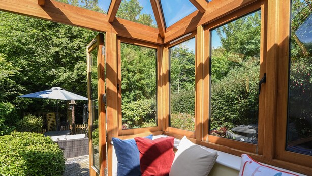 A wooden conservatory with a bench, pillows, and a cushion with 'SEA THE DAWN' text. - 21 Mill Green (Lyme Regis)