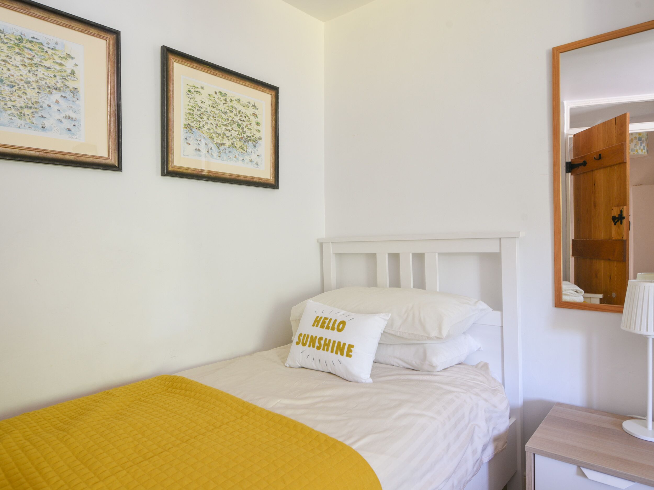A neatly arranged bedroom with a bed, a bedside table, a mirror, and two framed pictures on the wall.