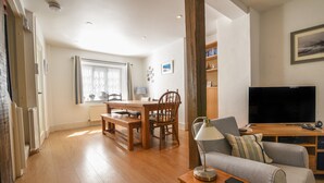 A living room with a wooden floor, a grey sofa, a wooden coffee table, a TV, and a bookshelf. - 21 Mill Green (Lyme Regis)
