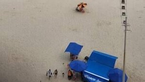 A beach with umbrellas and beach chairs, a lifeguard tower, and a clear view of the ocean. - Apartamento Guarujá (Guarujá)