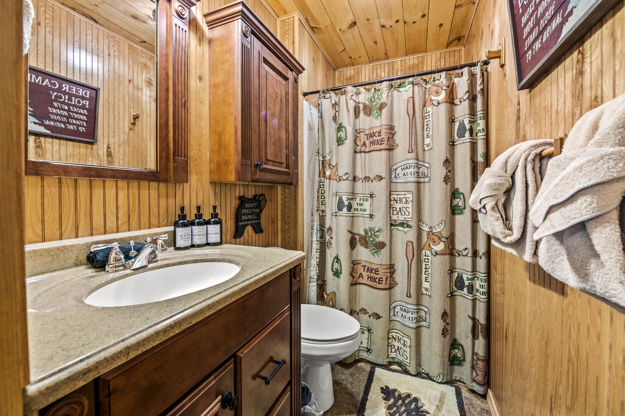 Un baño de madera con lavamanos, armarios y cortina de ducha con motivos de senderismo y camping.