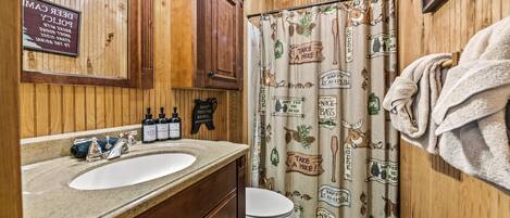 Un baño de madera con lavamanos, armarios y cortina de ducha con motivos de senderismo y camping.