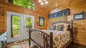 A wooden cabin bedroom with a bed, a dresser, and a door leading to a balcony.