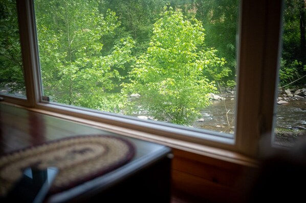 A room with a large window overlooking a forested area with a stream.