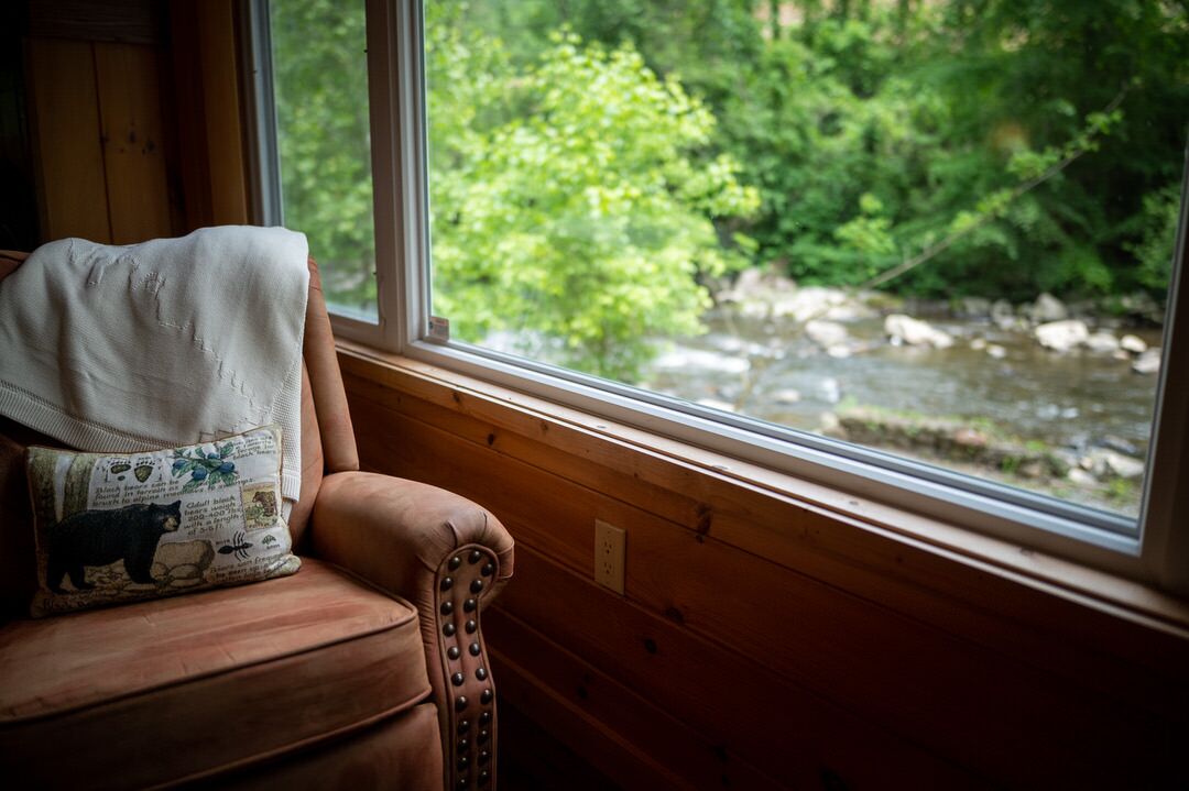 A wooden cabin interior with a window overlooking a river and forest.