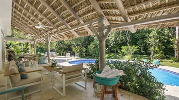 A covered outdoor area with a pool, seating, and a thatched roof structure.