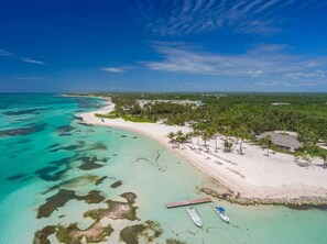 An aerial view of a beach with clear turquoise waters, a sandy shore, and a small dock with boats.