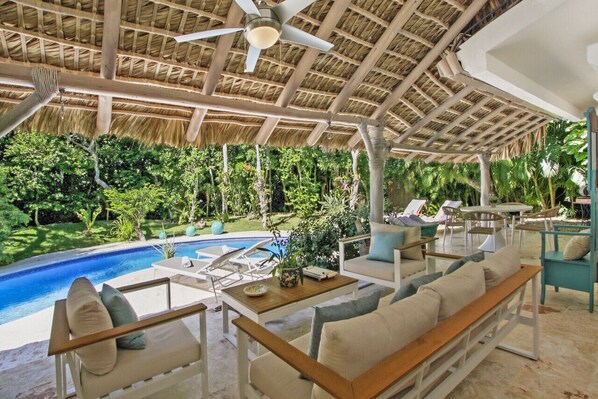 A poolside area with lounge chairs, a table, and a ceiling fan.