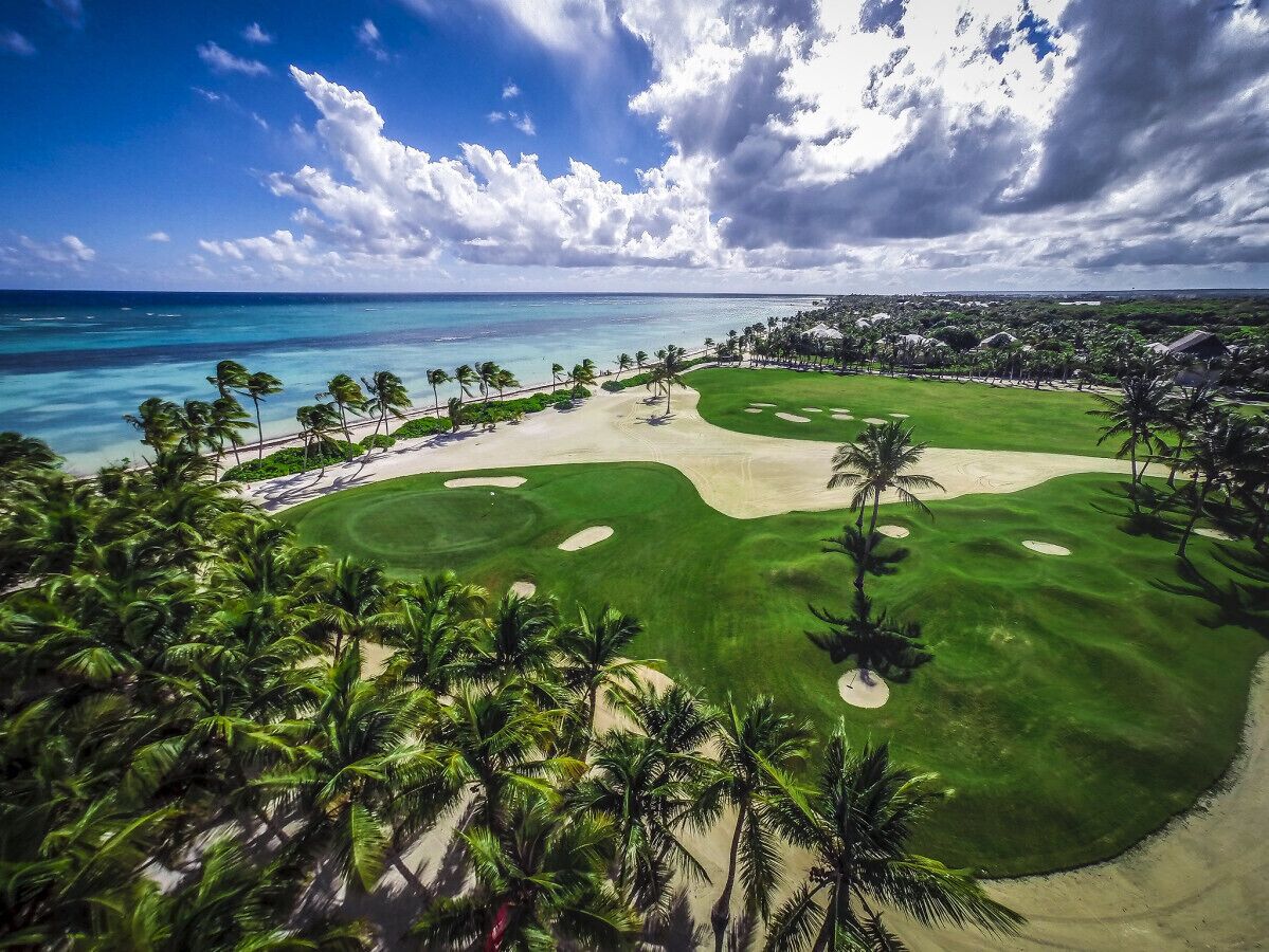 A golf course with a sandy area, palm trees, and a view of the ocean.
