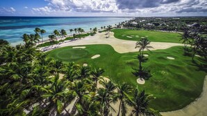 Een golfbaan met een zandgebied, palmbomen en uitzicht op de oceaan.
