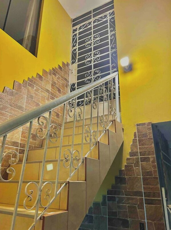 Una escalera con barandilla de metal y balaustres decorativos, que conduce a un rellano con un muro de diseño blanco y negro.