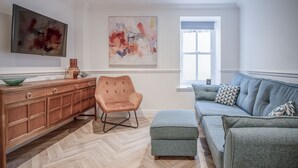 Uma sala de estar moderna com um armário de madeira, uma poltrona estofada, um sofá cinza e arte abstrata nas paredes.