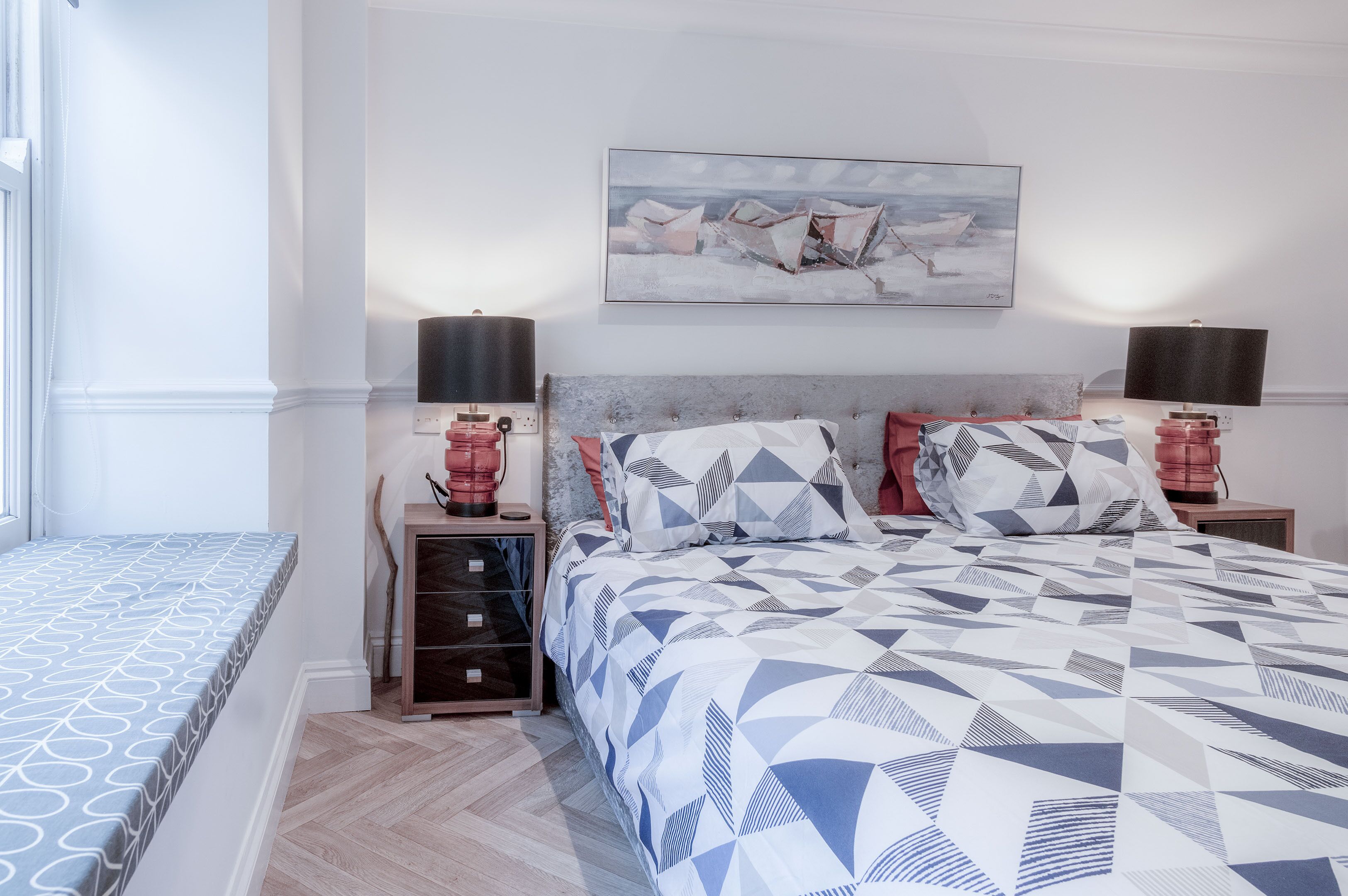 A bedroom with a bed, nightstands, a lamp, and a painting on the wall.
