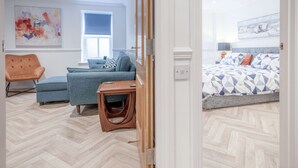 Quarto moderno com piso em padrão herringbone, cama com roupa de cama estampada, sofá azul, mesa de cabeceira de madeira e uma cadeira.