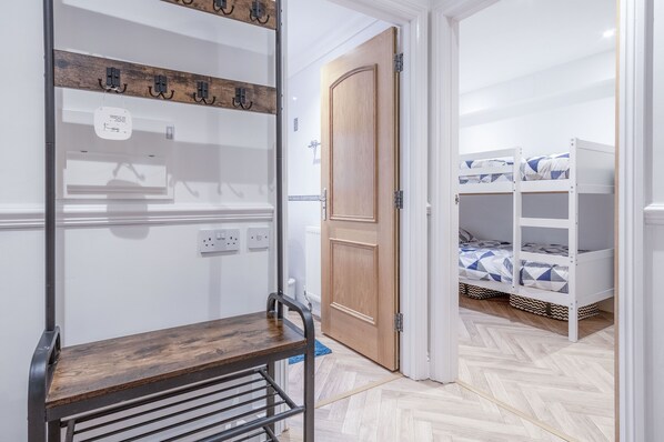 Une pièce avec des lits superposés, un banc en bois, un porte-manteau et une porte donnant sur une autre pièce.