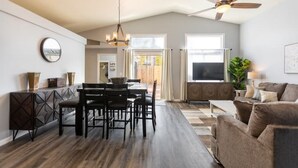 A spacious living area with a dining table and chairs, a sofa, a TV, and a ceiling fan.