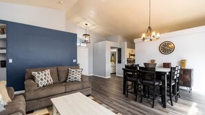 A modern living room with a sofa, coffee table, and dining area with chairs and a chandelier.