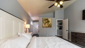 A hotel room with two beds, a ceiling fan, a painting, and a wardrobe.