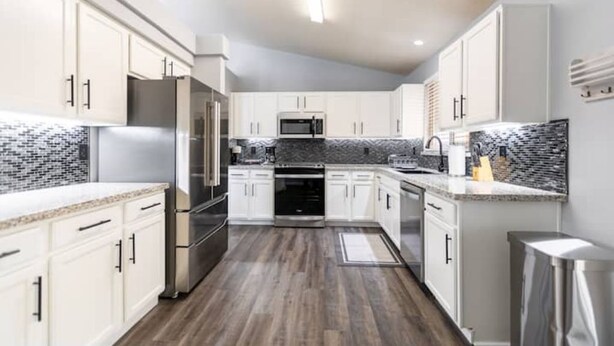 A modern kitchen with white cabinets, stainless steel appliances, and a black and white backsplash.