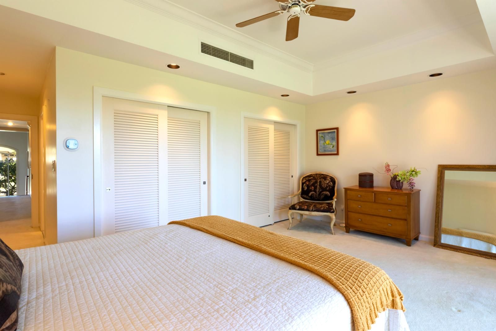 Une chambre à coucher comprenant un lit, une chaise, une commode, un miroir et un ventilateur de plafond.