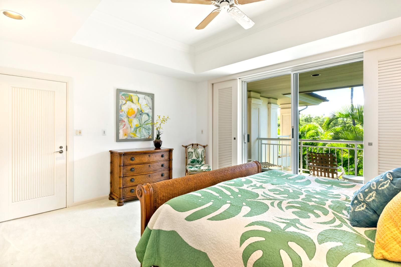 A bedroom with a bed, a dresser, a painting, and a sliding glass door leading to a balcony.