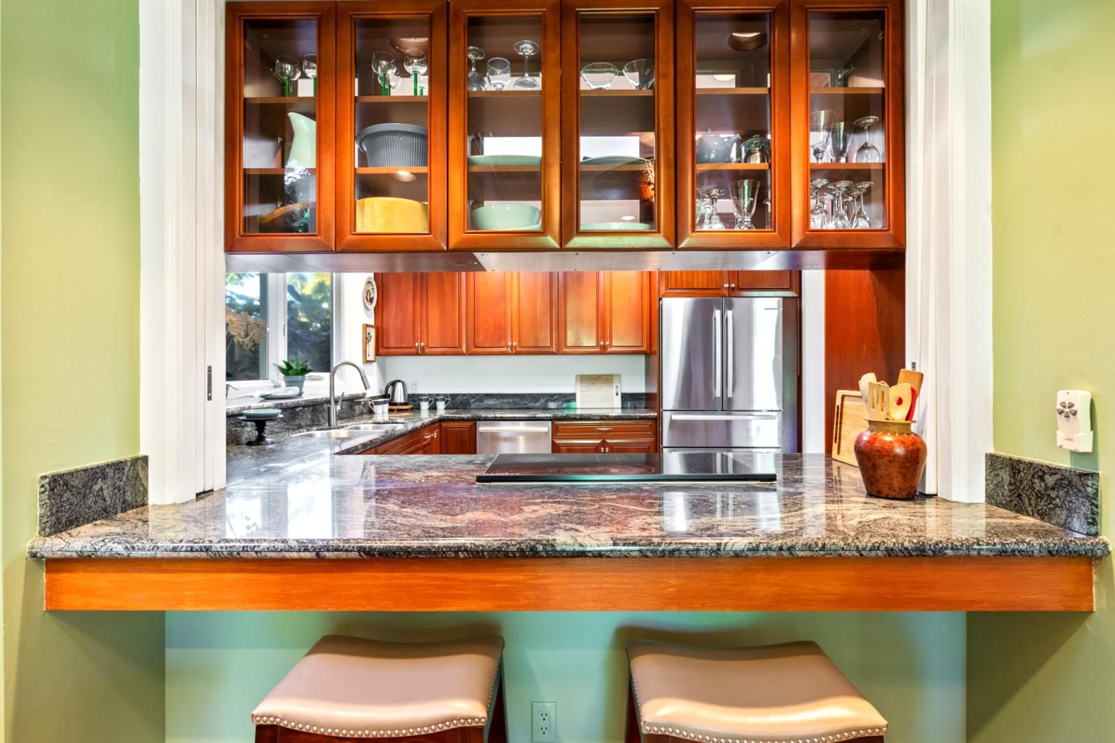 A kitchen with wooden cabinets, a stainless steel refrigerator, granite countertops, and a built-in island with stools.