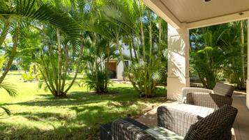 A covered outdoor seating area with wicker furniture, surrounded by lush greenery and palm trees.