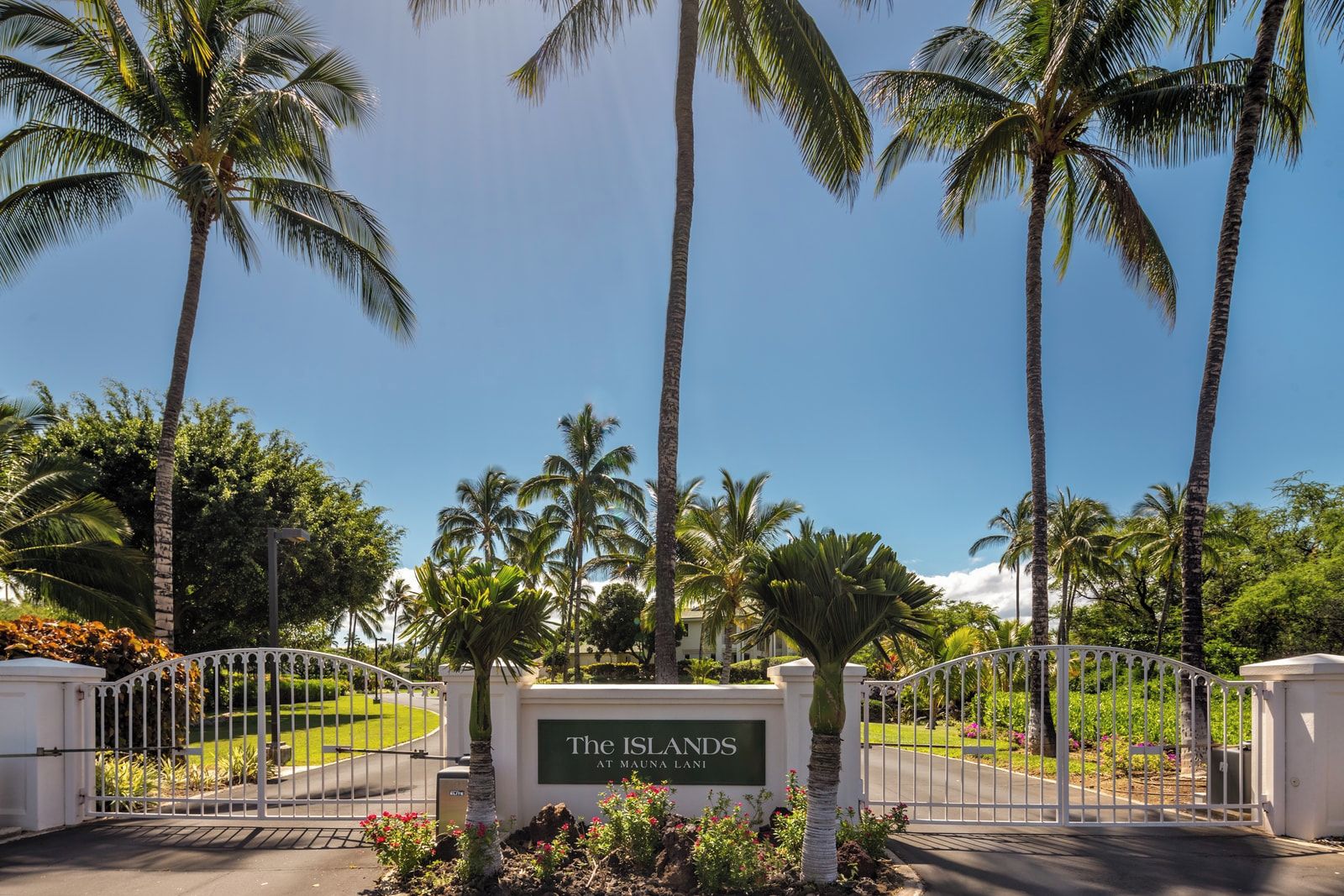 A gated entrance with a sign reading 'The ISLANDS at Mauna Lani' surrounded by palm trees and a well-maintained lawn.