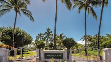 A gated entrance with a sign reading 'The ISLANDS at Mauna Lani' surrounded by palm trees and a well-maintained lawn.