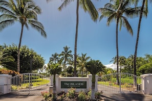Une entrée fermée par un portail, sur laquelle est apposée une plaque indiquant « The ISLANDS at Mauna Lani », le tout entouré de palmiers et d’une pelouse bien entretenue.