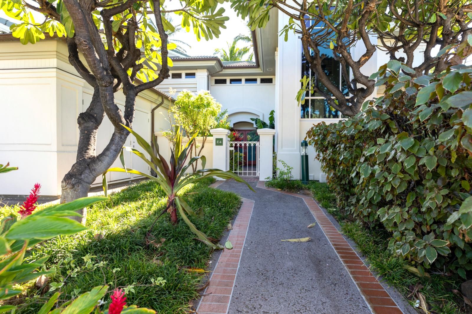 A pathway leading to a building with a gated entrance, surrounded by lush greenery and a well-maintained garden.