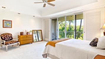 Un dormitorio con cama, cómoda, silla, ventilador de techo y balcón con vista a palmeras.