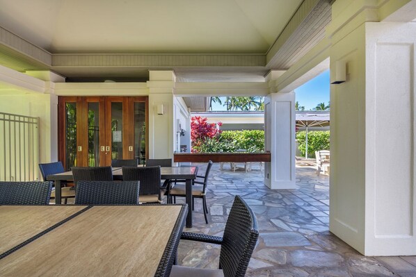 An outdoor patio area with a dining table and chairs, a wooden bench, and a view of a garden with red flowers.