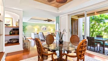 A dining area with a glass table, wooden chairs, and a view of the outdoors.
