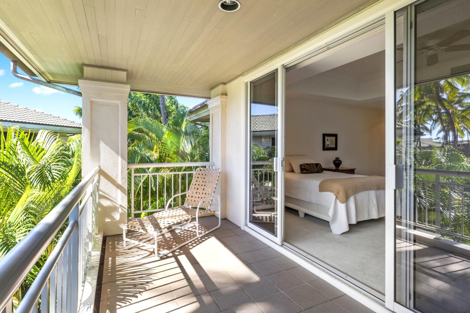 A balcony with a white chair and a bed with a white bedspread and a brown pillow.