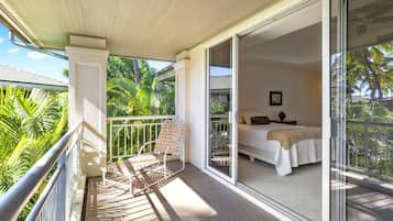 A balcony with a white chair and a bed with a white bedspread and a brown pillow.