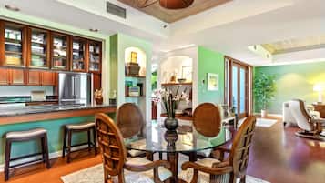 Un comedor con una mesa de vidrio rodeada de sillas de madera, una cocina con armarios de madera y una pared verde de acento.